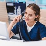 Young,Female,Receptionist,Talking,On,Phone,In,Clinic,While,Sitting