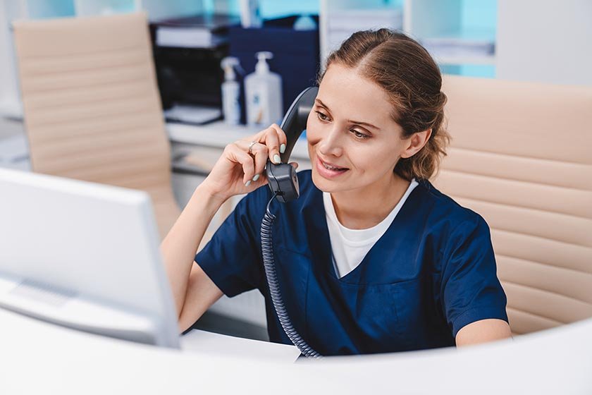 Young,Female,Receptionist,Talking,On,Phone,In,Clinic,While,Sitting